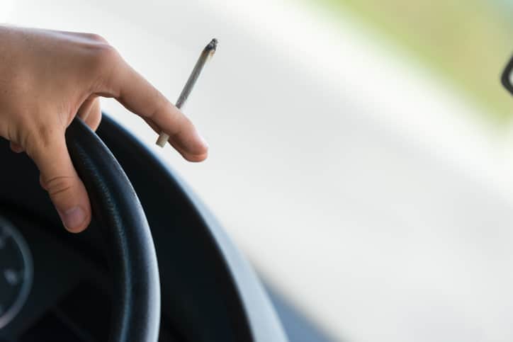 Close up of hand on car steering wheel holding a marijuana joint